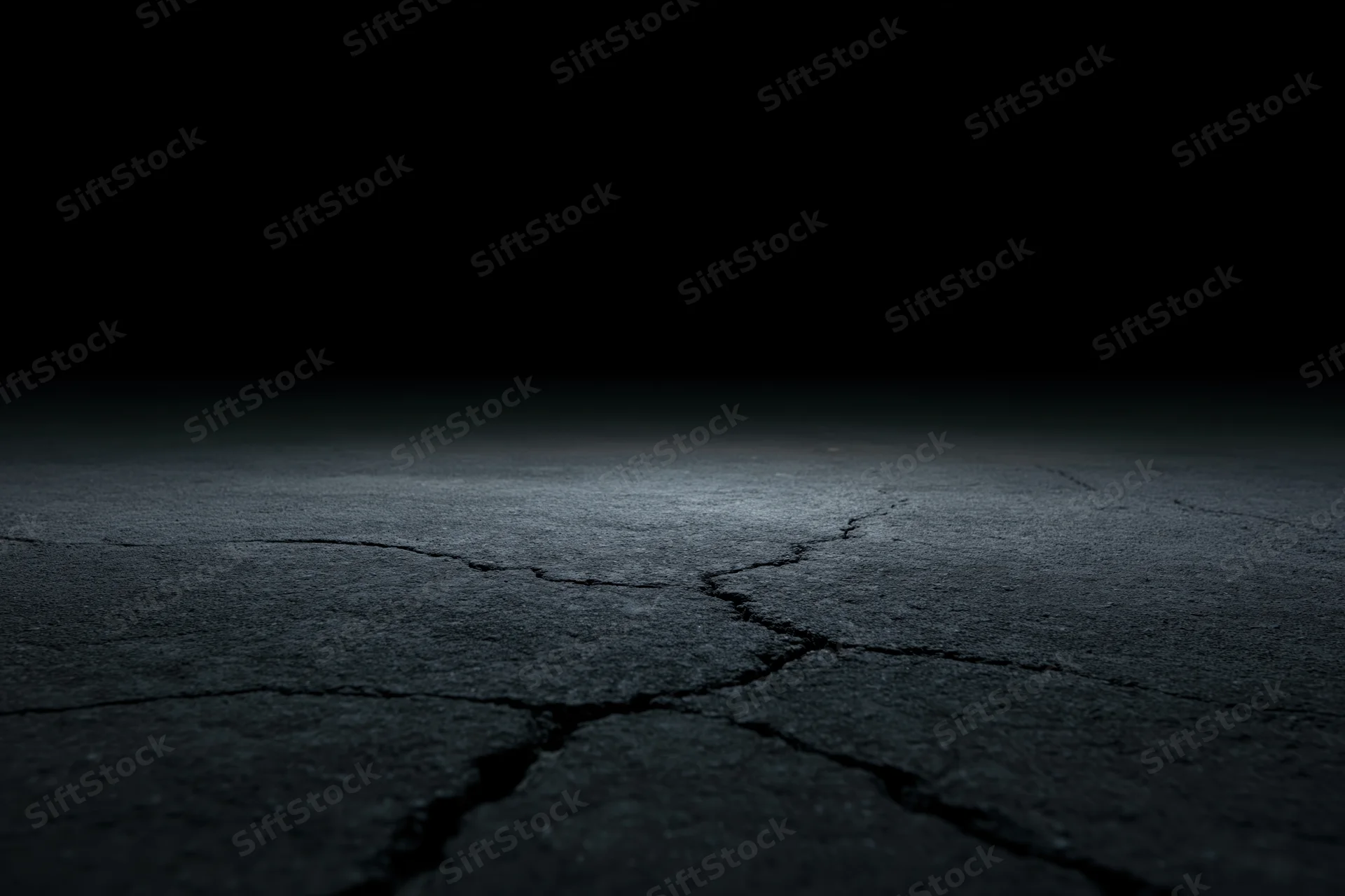 Cracked concrete floor fading into darkness from low angle wide view