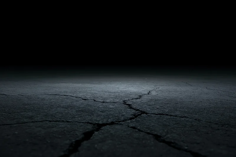 Cracked concrete floor fading into darkness from low angle wide view