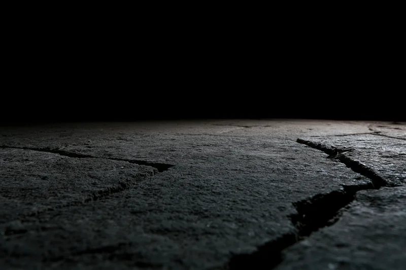 Cracked concrete floor fading into darkness from low angle wide view