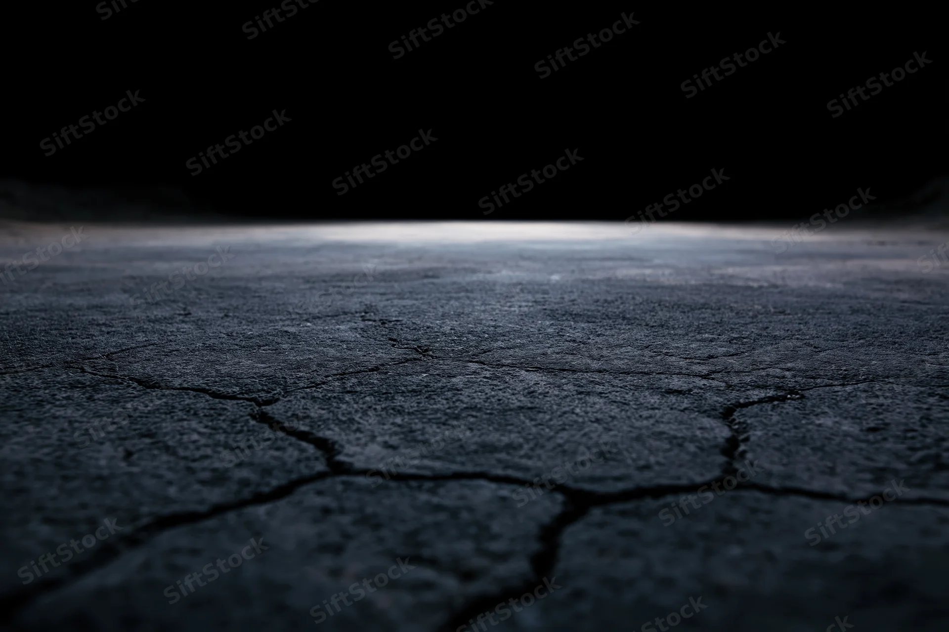 Cracked concrete floor fading into darkness at low angle