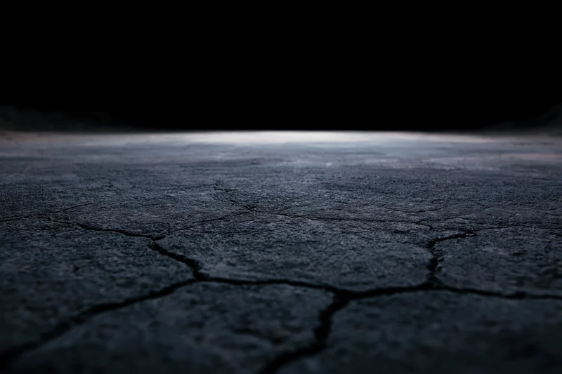Cracked concrete floor fading into darkness at low angle