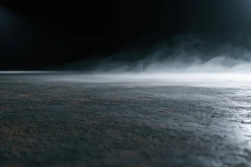 Dark empty concrete floor with low-lying smoke drifting across the surface