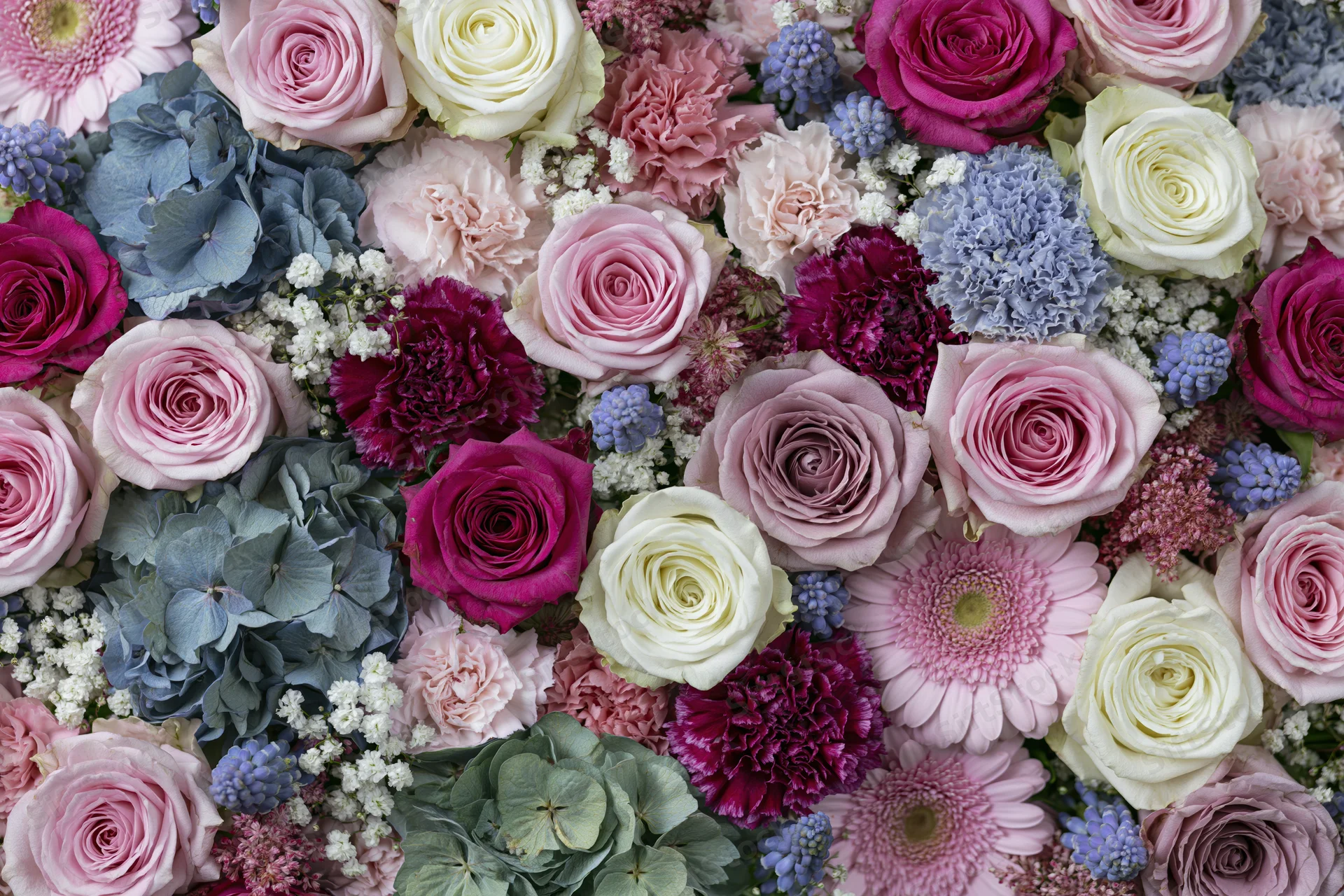 Dense flat-lay arrangement of mixed cut flowers including roses, hydrangeas, carnations, and gerberas in pink, white, purple, and blue hues