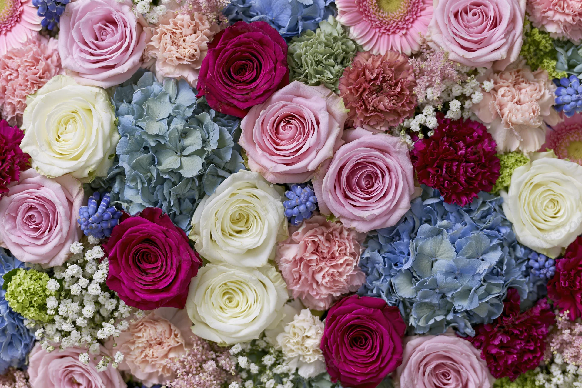 Dense flat-lay arrangement of mixed cut flowers including roses, hydrangeas, and carnations in pink, white, purple, and blue hues