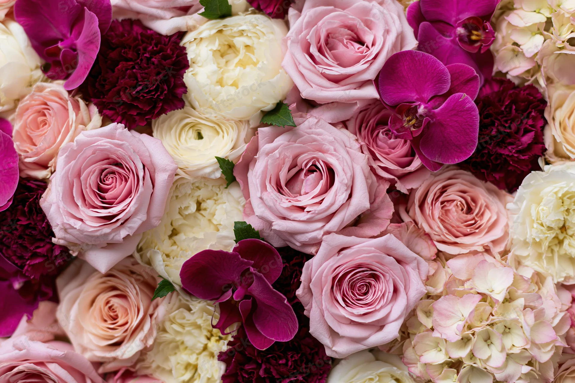 Dense flat-lay arrangement of mixed cut flowers including roses, orchids, carnations and hydrangeas in pink, white and purple hues