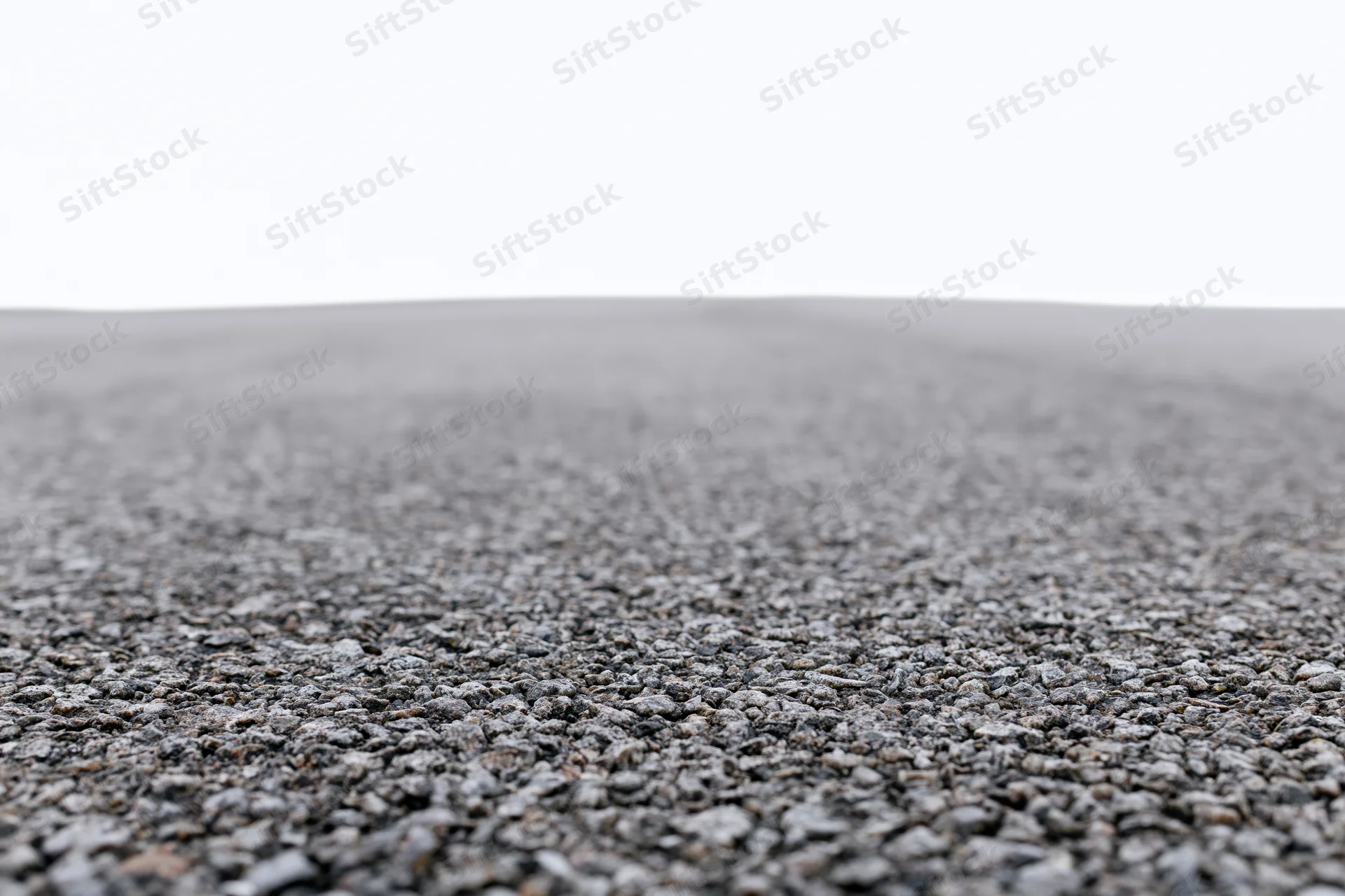 Asphalt road surface filling lower half of frame with white sky above