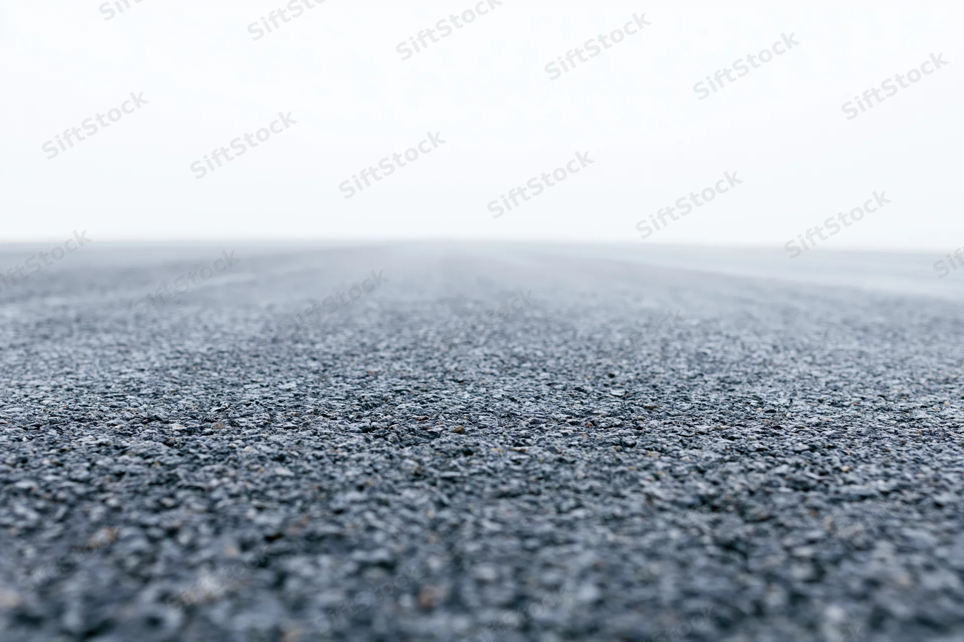 Asphalt road surface filling lower half of frame with shallow depth of field and vanishing point in distance