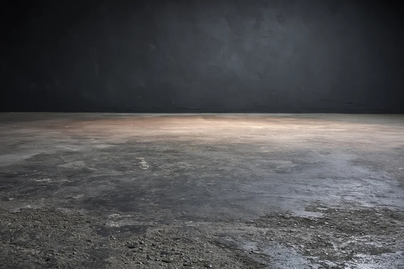 Empty concrete floor meeting dark bare plaster wall in industrial interior space