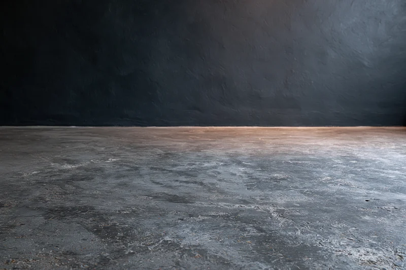 Empty concrete floor meeting dark bare plaster wall in industrial interior space