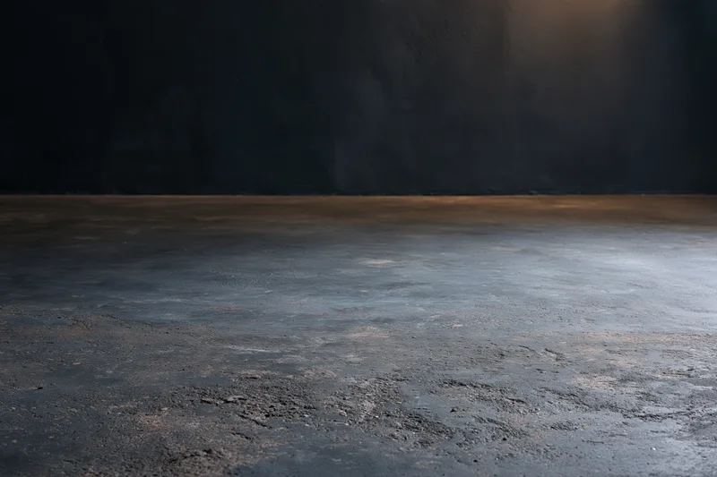 Empty concrete floor meeting dark bare plaster wall in industrial interior space