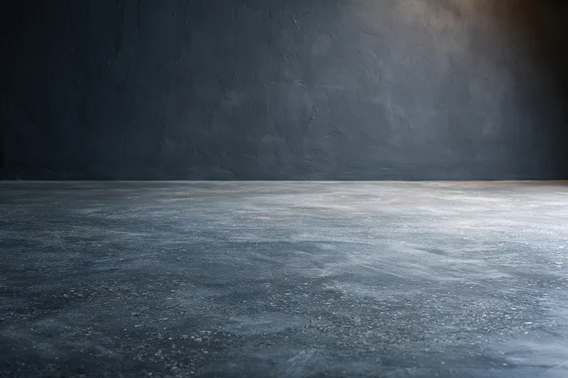 Empty concrete floor meeting dark bare plaster wall in industrial interior space