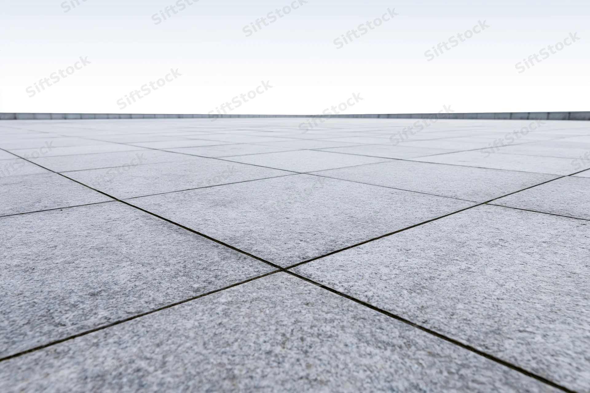 Concrete tile plaza floor stretching to white horizon in low-angle wide view