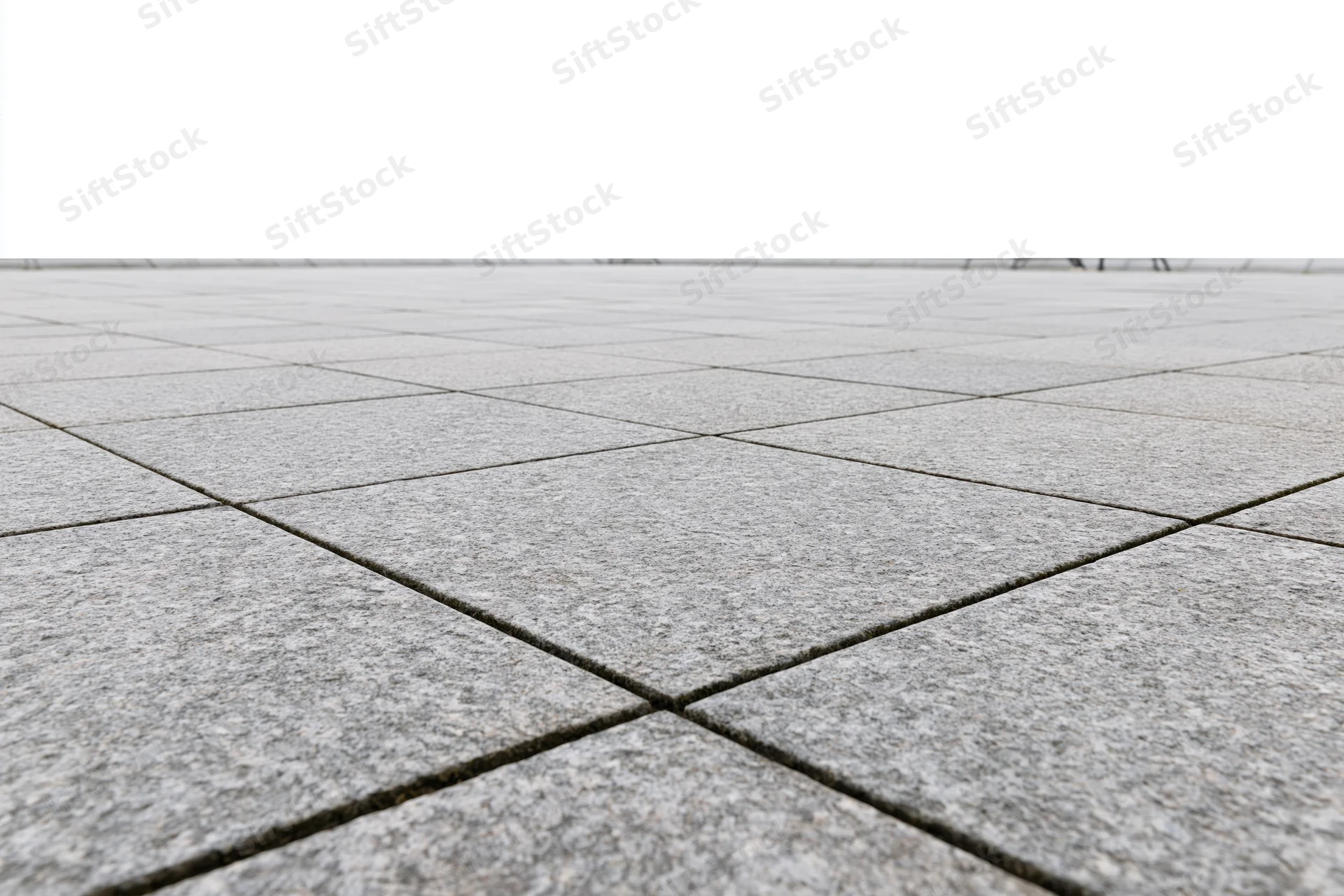Gray concrete tiles arranged in a grid pattern across an outdoor plaza floor stretching to a white horizon