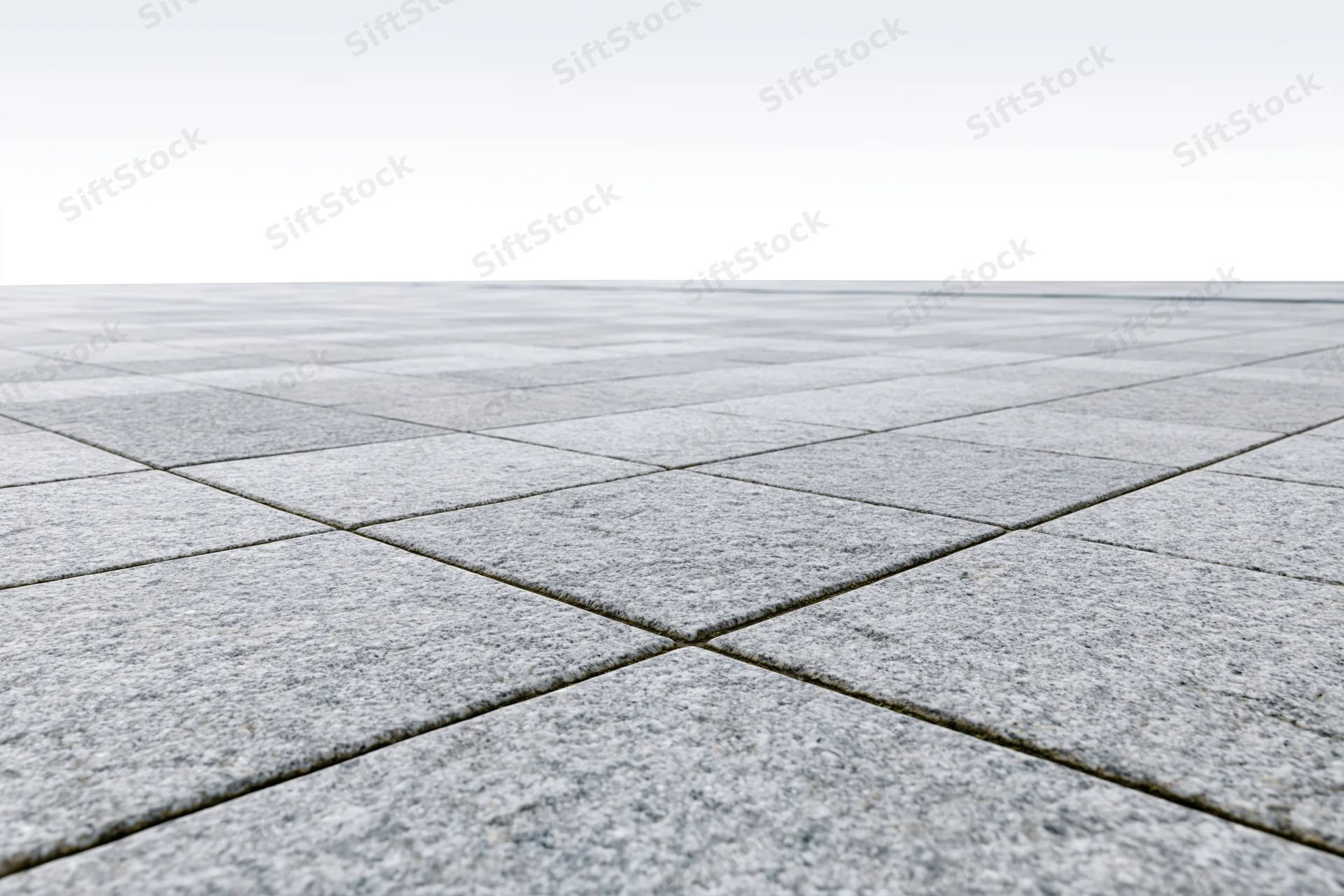 Gray concrete tiles arranged in a grid pattern on an empty outdoor plaza floor stretching to a white horizon