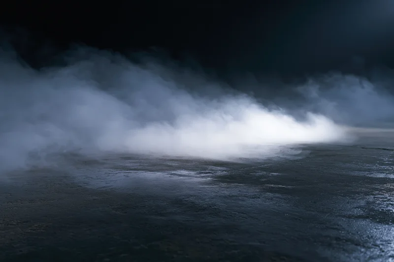 Thick white smoke drifting across a dark concrete floor in an empty industrial space