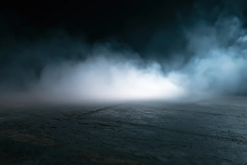 Thick white smoke drifting over dark concrete floor at night