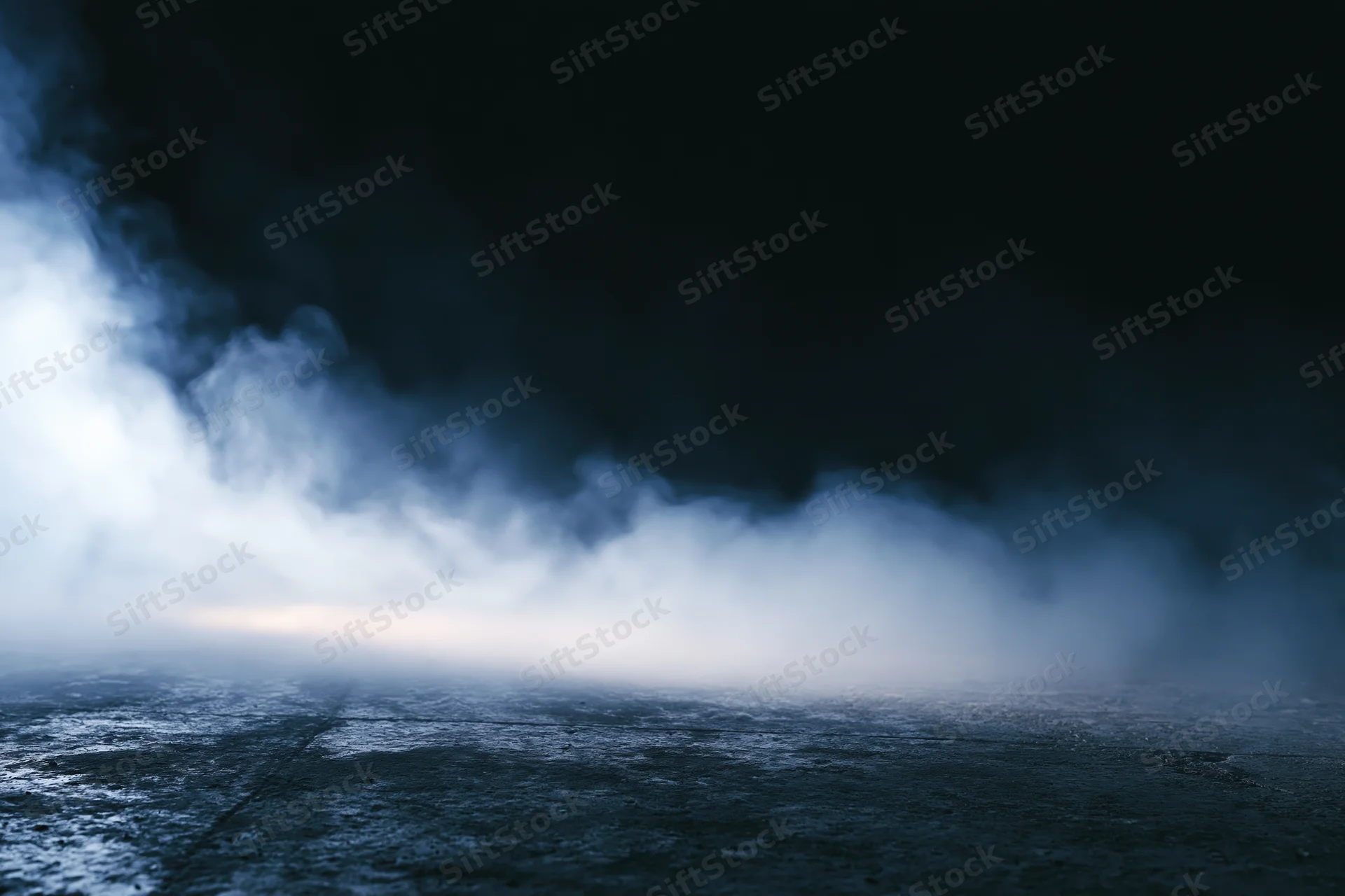 Thick white smoke drifting over dark concrete floor at night