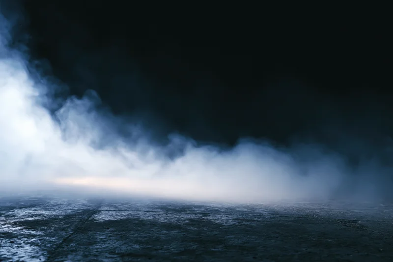 Thick white smoke drifting over dark concrete floor at night