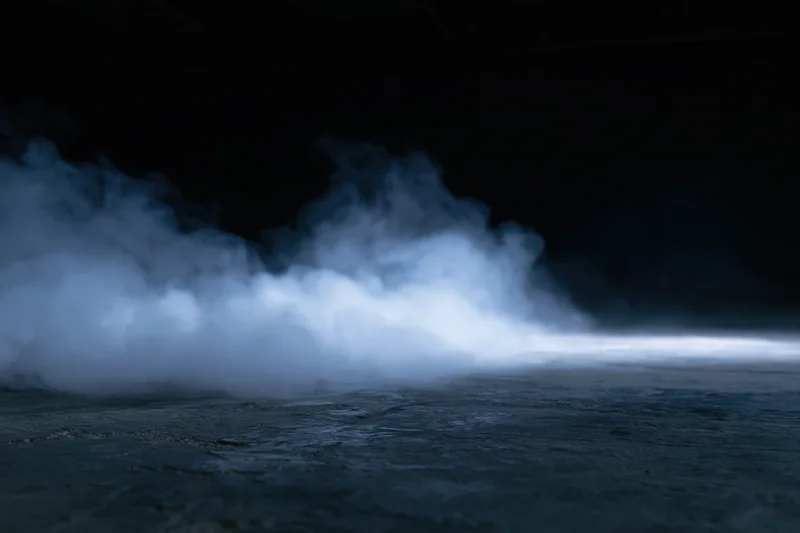 Thick white smoke drifting across dark concrete floor in industrial space