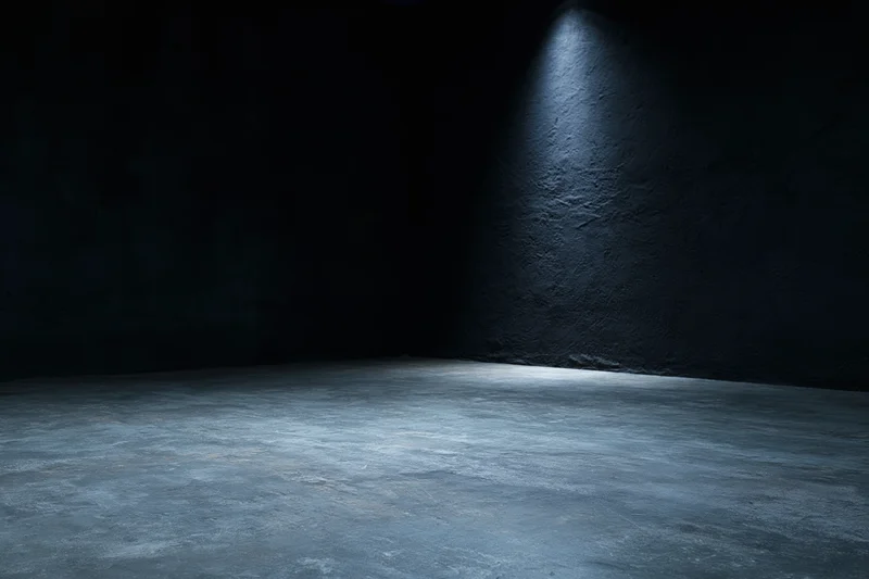 Empty dark studio interior with concrete floor and spotlight on rough wall