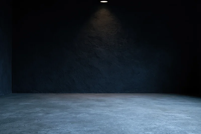 Empty dark studio interior with rough concrete floor and wall under spotlight