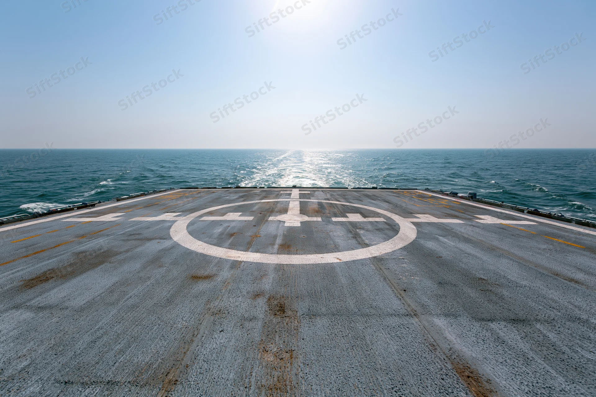 Helicopter landing pad on naval ship stern deck over ocean under bright sun
