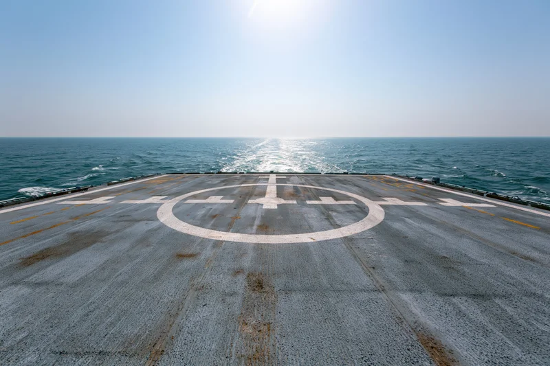 Helicopter landing pad on naval ship stern deck over ocean under bright sun