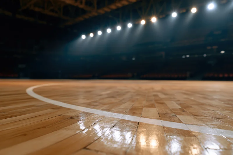 Low-angle view of empty indoor basketball court with polished wooden floor and spotlight lighting