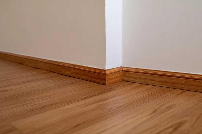 Interior corner with off-white painted walls and wooden baseboard trim meeting laminate flooring