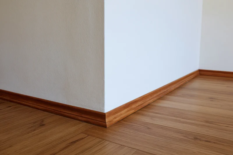 Empty room corner with white painted walls and bamboo flooring featuring wooden baseboard trim