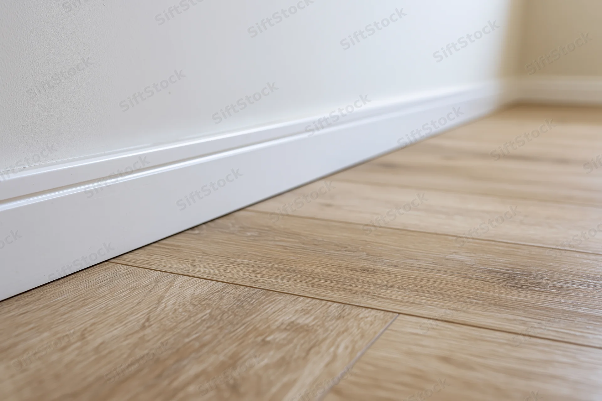 Light oak laminate flooring in a room corner with white baseboard and wall
