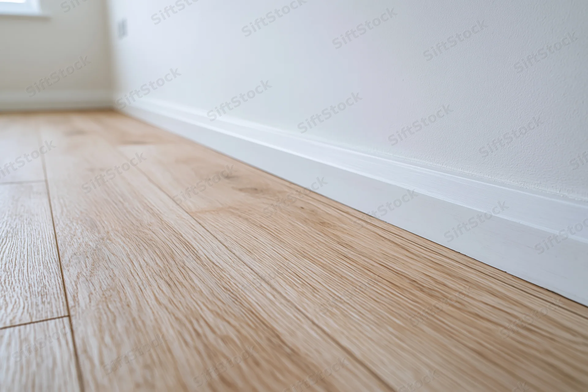 Light oak laminate flooring along white wall baseboard in empty room corner