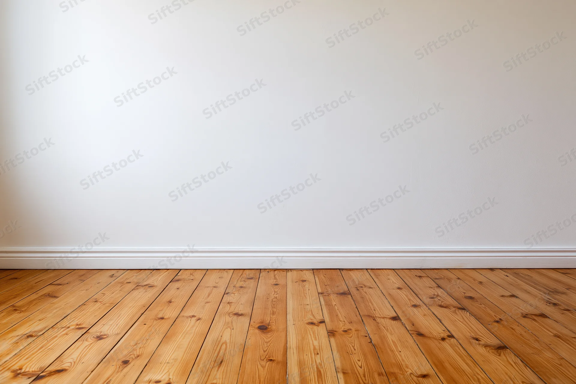 Empty room with plain white wall and bare wooden floor showing baseboard and wood grain texture