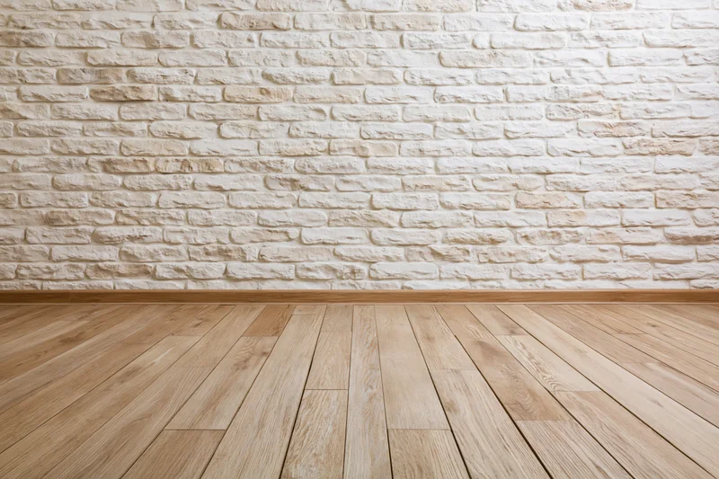 Empty interior room with whitewashed stacked stone brick wall and light wood plank flooring