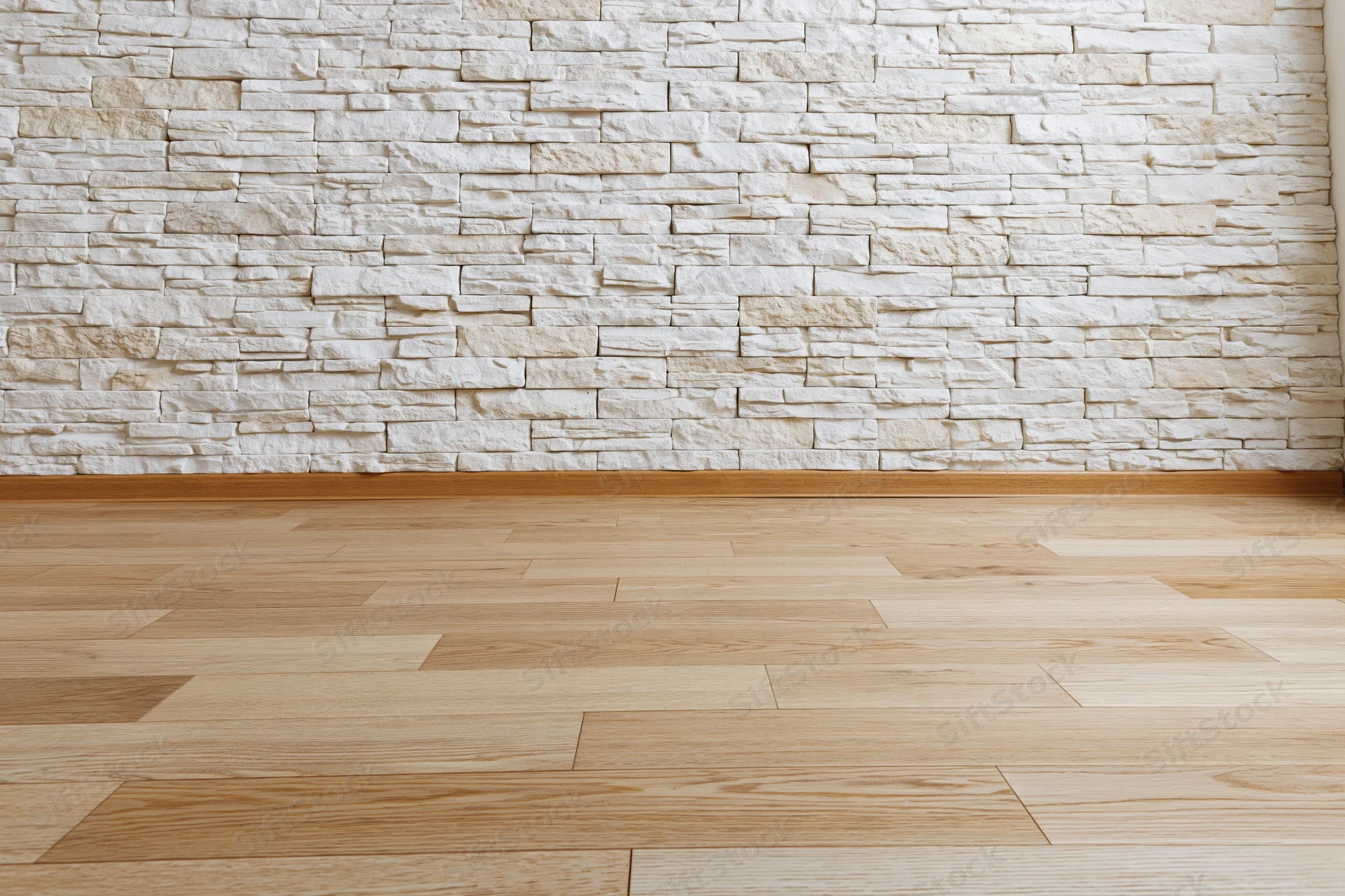 Empty interior room with whitewashed stacked stone wall and light wood flooring