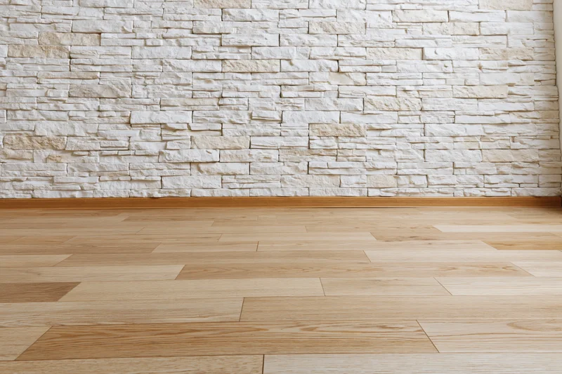 Empty interior room with whitewashed stacked stone wall and light wood flooring