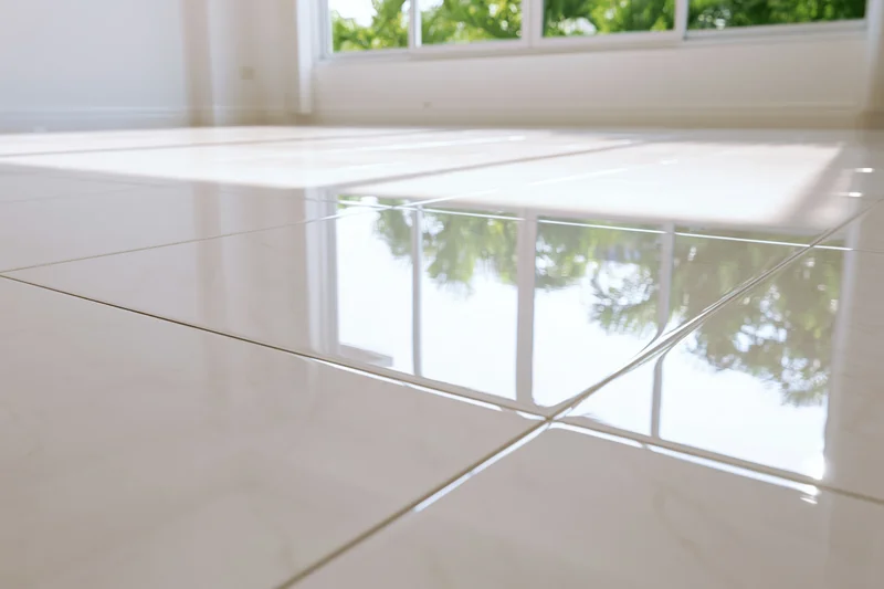 Glossy white polished tile floor reflecting window and greenery in empty interior room