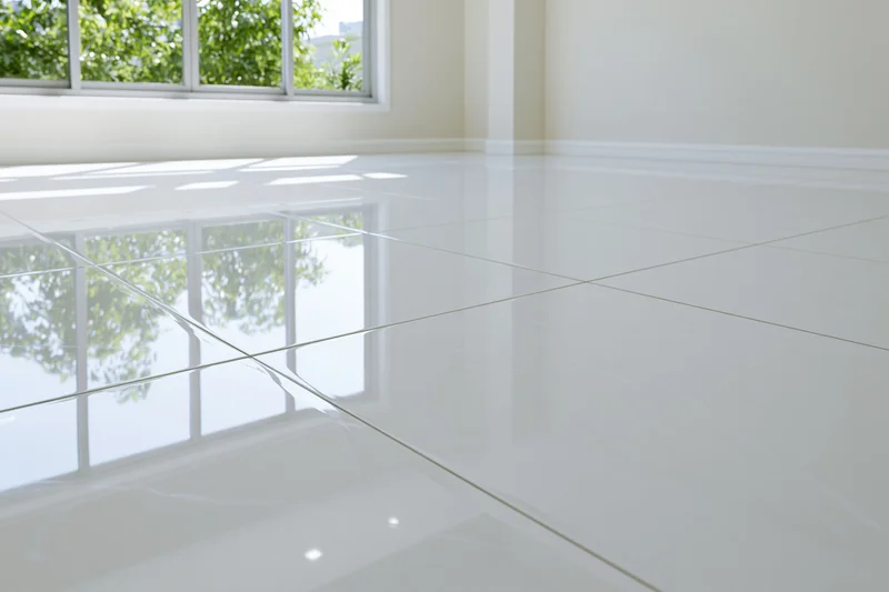 Glossy white polished tile floor reflecting window and greenery in empty interior room