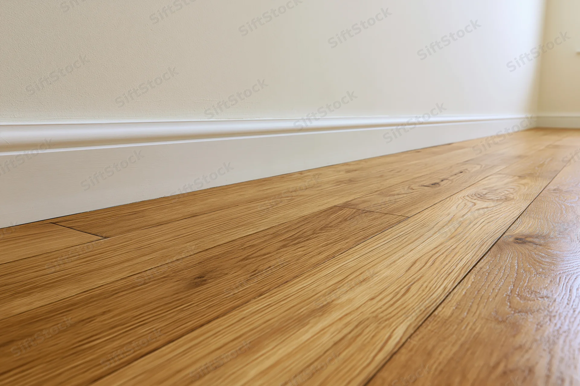 Warm oak parquet flooring meeting a beige wall with white baseboard in an empty interior room