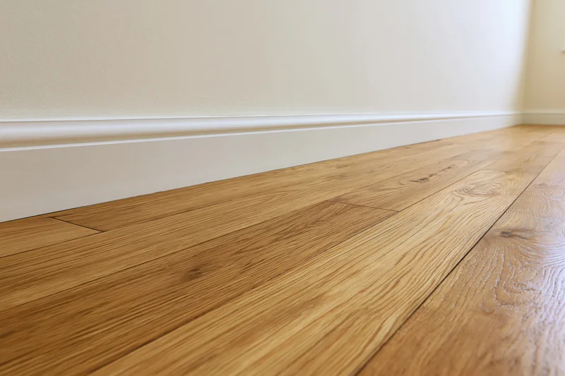 Warm oak parquet flooring meeting a beige wall with white baseboard in an empty interior room