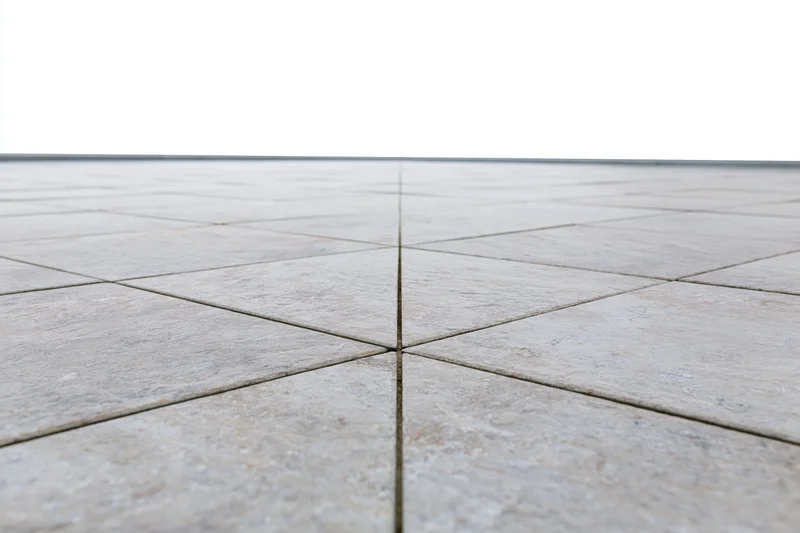 Light grey stone tile floor arranged in square pattern receding into perspective with visible grout lines