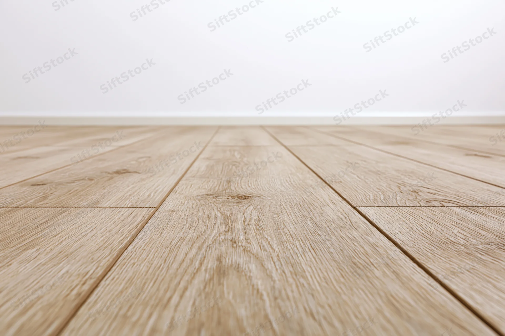 Light oak wood plank floor stretching toward a plain white wall in an empty interior space