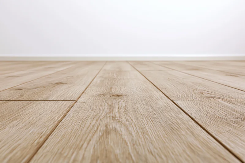 Light oak wood plank floor stretching toward a plain white wall in an empty interior space