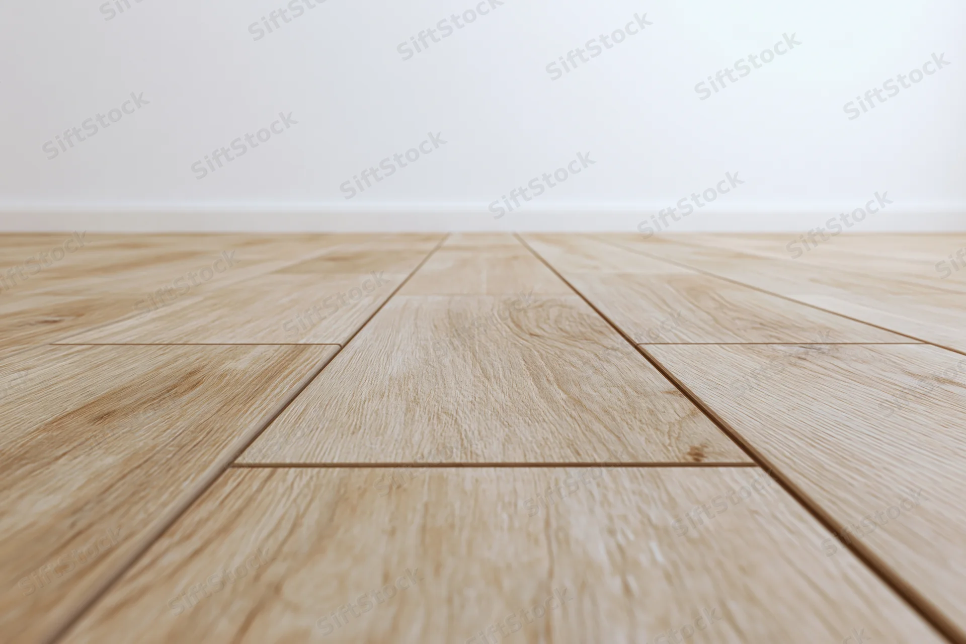 Light oak wood plank floor stretching toward a plain white wall in an empty interior space