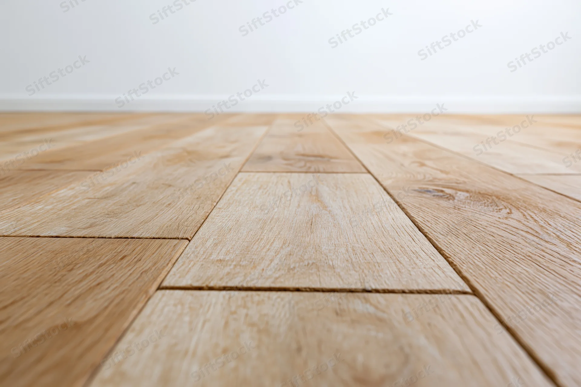 Light oak wood plank floor stretching toward a plain white wall in an empty room