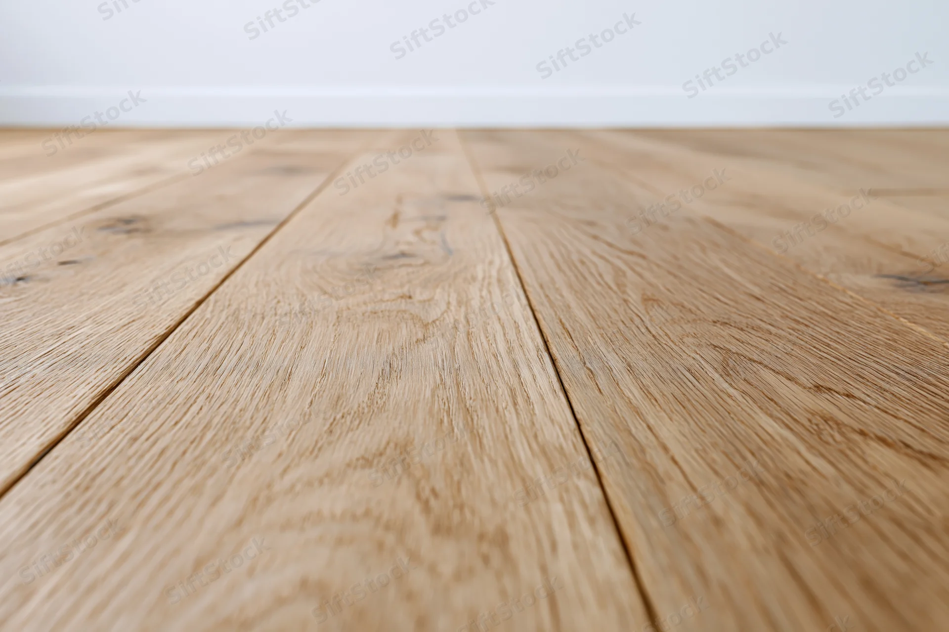 Light oak wood plank floor stretching toward a plain white wall in an interior space