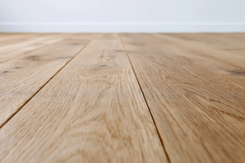 Light oak wood plank floor stretching toward a plain white wall in an interior space