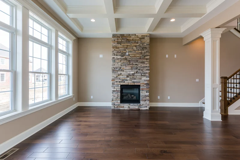 Empty living room with stone fireplace and dark hardwood flooring in a newly built home