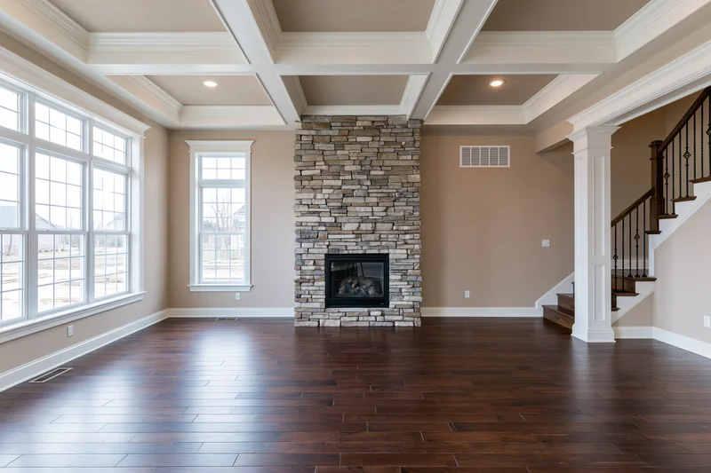 Empty living room with stone fireplace and dark hardwood flooring in newly built home