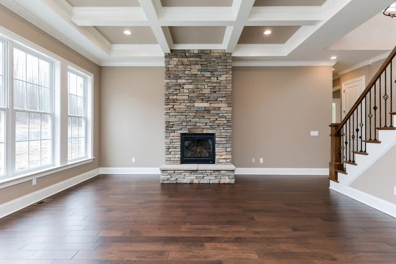 Empty living room with stone fireplace and dark hardwood flooring in newly built home